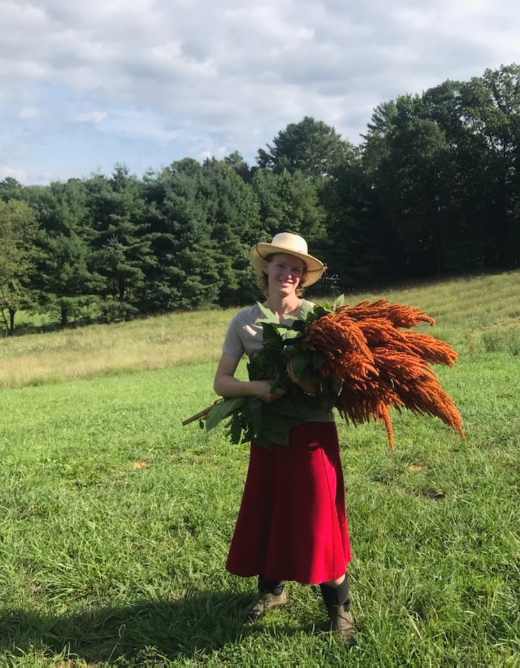 Amy, owner of Stalk Market Flower Farms is pictured standing in a field holding a bundle of large orange flowers